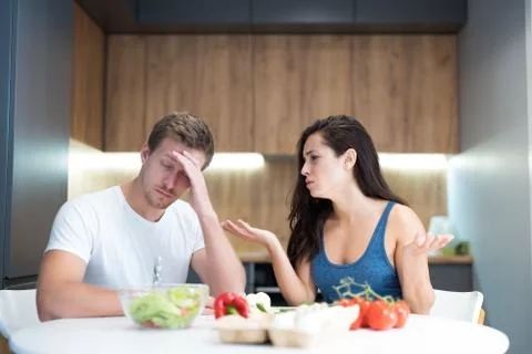 Young couple having fight while cooking breakfast in the kitchen husband looks Stock Photos