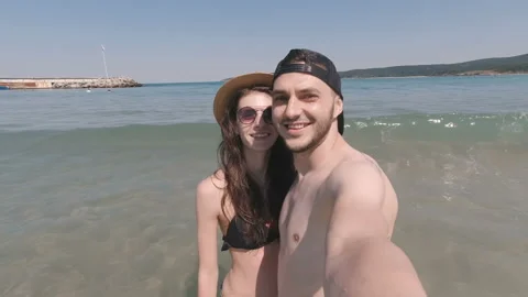 Young couple having fun at the beach. Sea waves crashing at them Stock Footage 136037795