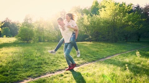 Young couple having fun in spring park. Girl riding her boyfriend's back Stock Footage 89520936