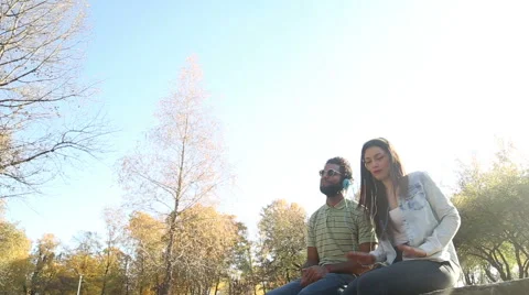 Young couple having fun while listening to music on headphones in park Stock Footage 59554782