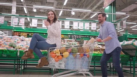Young couple having fun while choosing food in the supermarket, man pushing Stock Footage 124789911