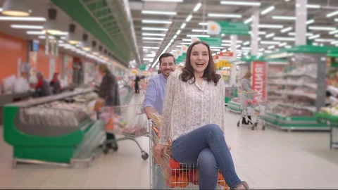 Young couple having fun while choosing food in the supermarket, man pushing Stock Footage 127843589