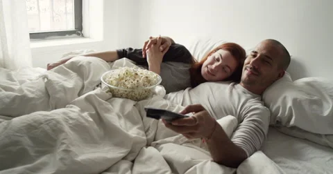 Young couple having popcorn while watching television in bedroom Vídeo Stock 63374340