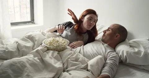 Young couple having popcorn while watching television in bedroom Vídeo Stock 63374362