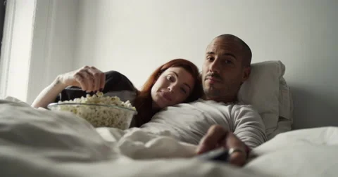 Young couple having popcorn while watching television in bedroom Vídeo Stock 63374372