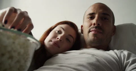 Young couple having popcorn while watching television in bedroom Vídeo Stock 63374391