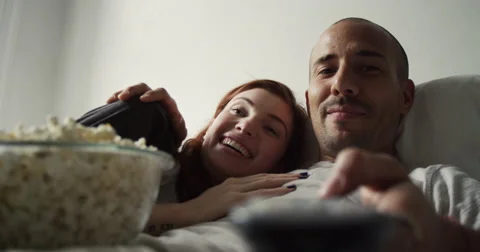 Young couple having popcorn while watching television in bedroom Vídeo Stock 63374406