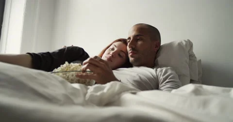 Young couple having popcorn while watching television in bedroom Vídeo Stock 63374421