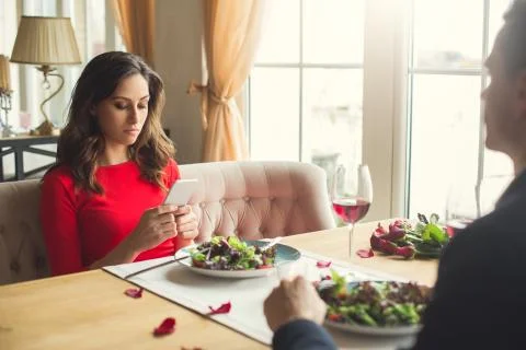 Young couple having romantic dinner in the restaurant using smartphone bored Stock Photos