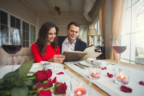 Young couple having romantic dinner in the restaurant holding menu choosing Stock Photos