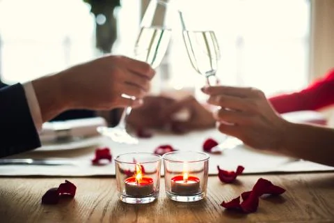 Young couple having romantic dinner in the restaurant drinking champagne cheers Stock Photos