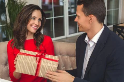 Young couple having romantic dinner in the restaurant holding a present grateful Stock Photos