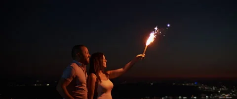 Young couple holding a firework on the hill at night, with bokeh city lights  Stock Footage 136239976