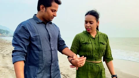 Young couple holding hands walking and talking on the sandy beach Stock Footage 263486941