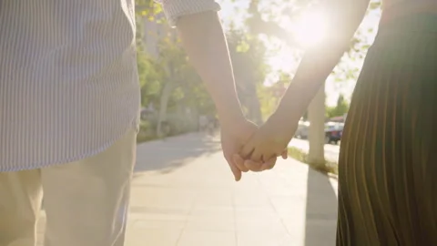 Young couple holding hands while walking down a sunny street Stock Footage 303854485