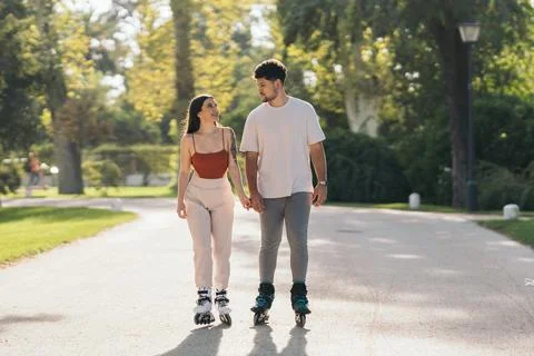Young couple holding hands while skating in a path of a park Stock Photos
