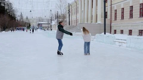 Young couple holding hands while ice skating, gliding together on snow covered Stock Photos