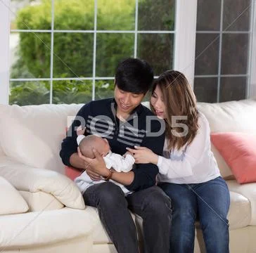 Young couple holding their infant son on white sofa Stock Photos