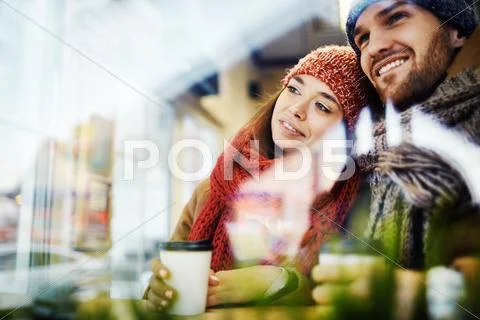 Young couple with hot drinks looking through window in cafe Stock Photos