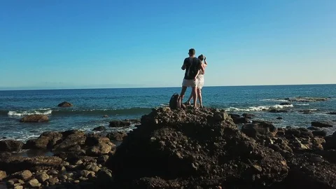Young couple hugging, looking at the ocean. Woman raises her hand up. Back view Stock Footage 95406064