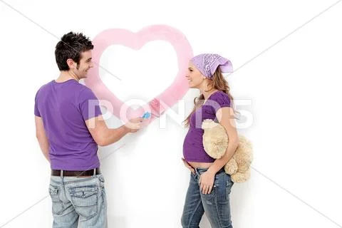 Young couple, husband and pregnant wife painting nursery wall. Stock Photos