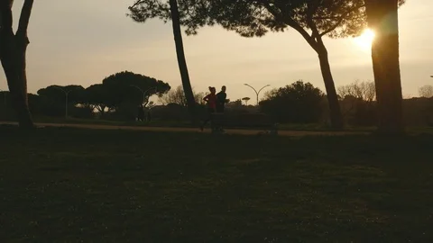 A young Couple jog in a park, high contrast silhouette at sunset. Stock Footage 104048232