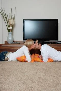 Young couple kissing in front of TV set Stock Photos