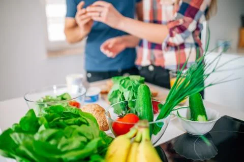 Young couple in the kitchen. On the first plan vegetables and fruits on the t Stock Photos