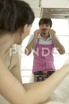 Young couple in kitchen, man holding chilli to nose Stock Photos
