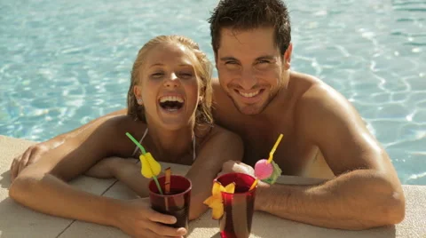 Young couple laughing with drinks at side of pool Stock Footage 43624648