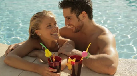 Young couple laughing with drinks at side of pool Stock Footage 43624670