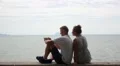 Young Couple Laughing with Mobile Phone against the Sea. HD Footage