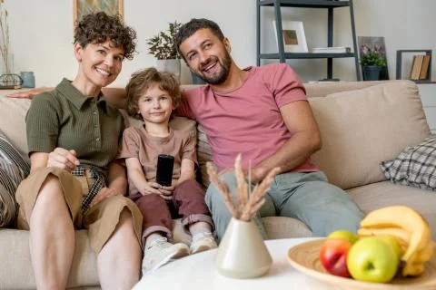 Young couple laughing at tv program with their little son sitting between them Fotos de archivo