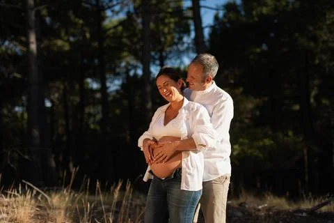 Young couple laughs together while caressing mom's belly and their future child Stock Photos