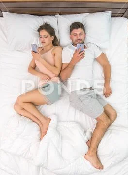 The young couple lay on the bed and phone. View from above Stock Photos