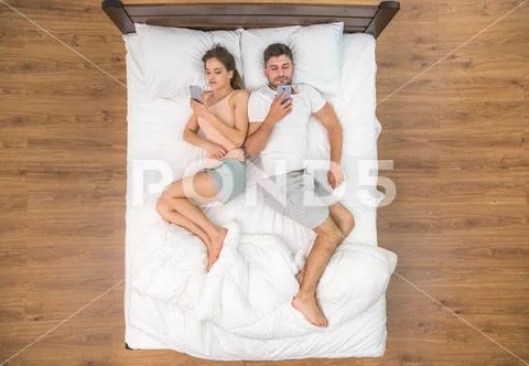 The young couple lay on the bed and phone. View from above Stock Photos