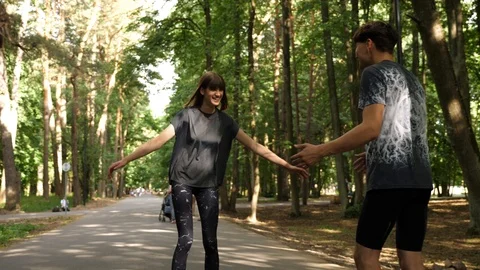 Young couple learning how to skate with roller blades in the park, boyfriend try Stock Footage 91706071
