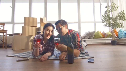 Young couple lies on the floor drinking wine and notes moving into a new Stock Footage 89455376