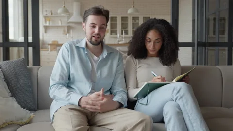 Young Couple in Light Clothes Sit on Sofa and Discuss Joint Plans for Future Stock Footage 298183365