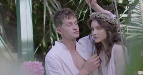 Young couple in light robes on swing among garden Stock Footage 247814073