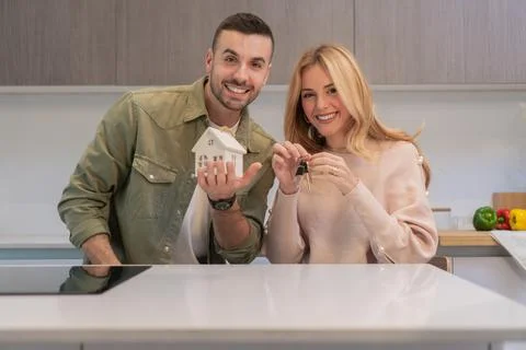 Young couple looking at camera and smiling, the woman is holding the key of a Stock Photos