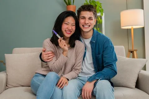 Young couple looking at camera sitting on the sofa smiling holding a pregnancy Stock Photos