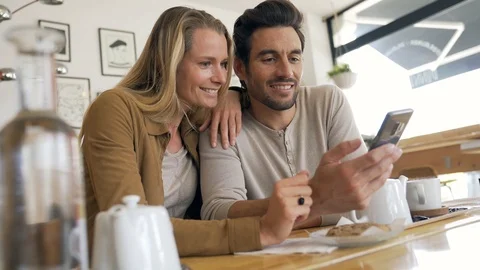 Young couple looking at a cell phone in a coffee shop Stock Footage 118901537