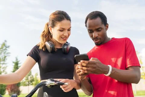 Young couple looking at smartphone while standing with bicycles in park, soci Фото