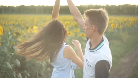 Young couple in love dancing in the evening at sunset in a field of sunflowers. Video stock 100379397
