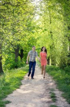 A young couple in love, a guy and a girl, run along the park alley towards th 写真素材