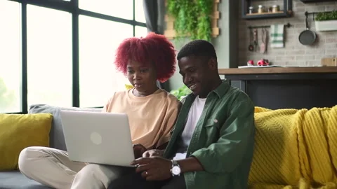 Young couple in love using laptop and watching web or video, sitting on sofa in Stock Footage 166014839