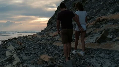 Young couple in love walking in evening on a rocky beach. Stock Footage 80316652