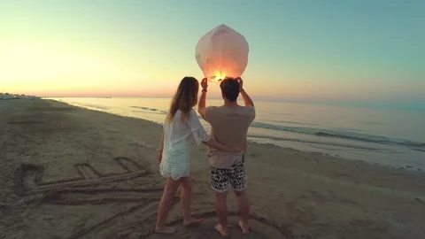 Young couple of lovers lighting sky lantern on the beach at sunset Stock Footage 137440711