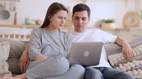 Young couple in loving relationship talking and using laptop, sitting on couch Stock Footage 165792772